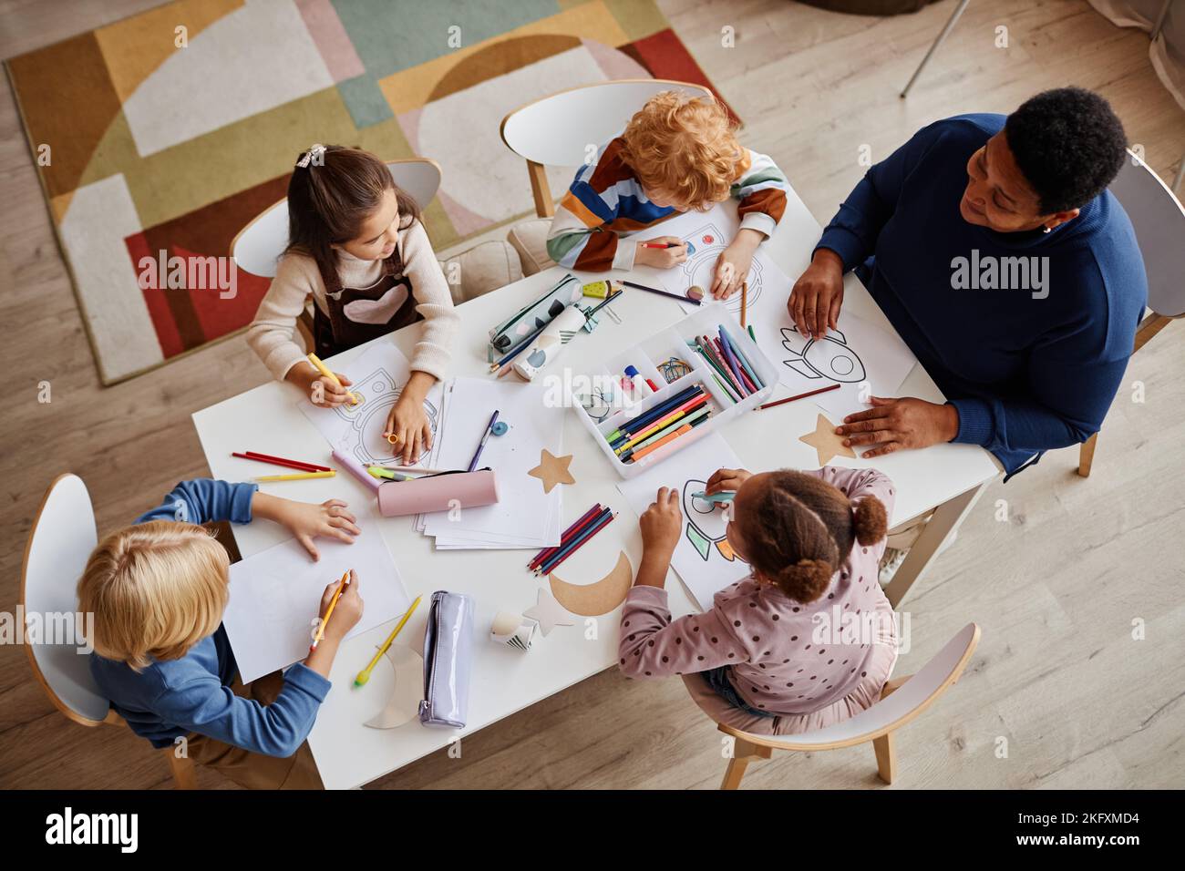Photo ci-dessus de plusieurs apprenants interculturels de l'école maternelle et de leur enseignant assis devant eux pendant la leçon de dessin Banque D'Images