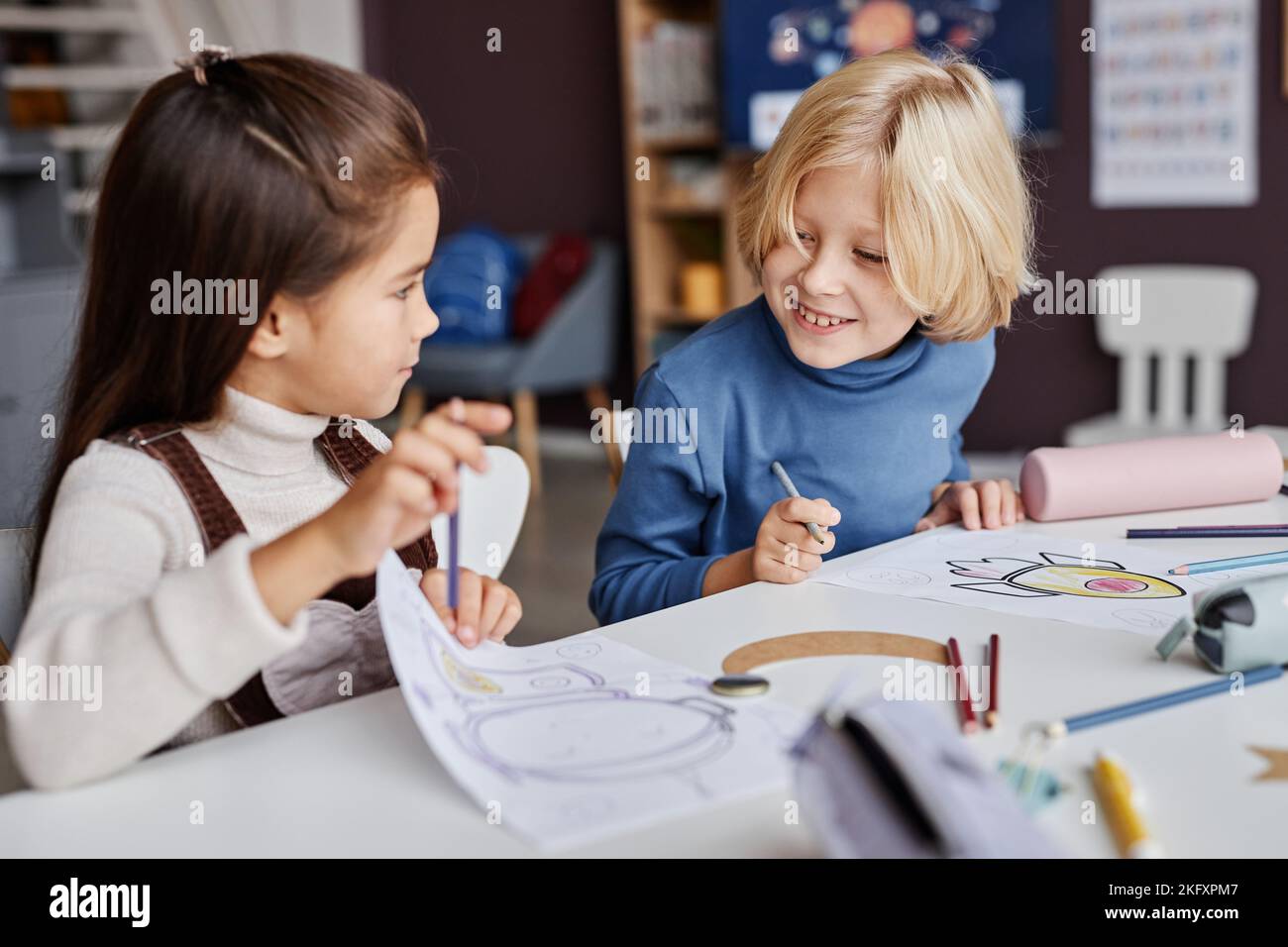 Petit garçon blond regardant l'image dessinée et tenue par son camarade de classe le lui montrant à la leçon de dessin à l'école maternelle Banque D'Images