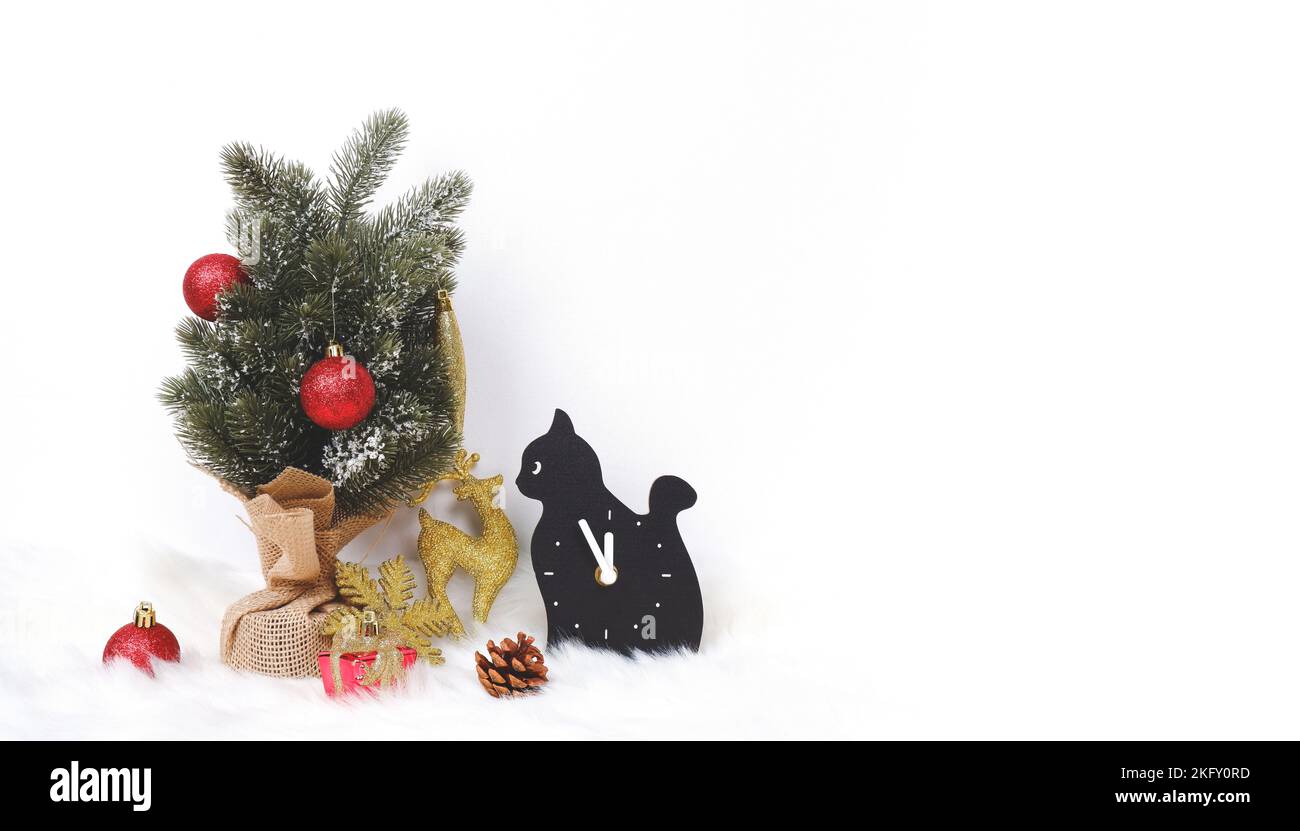 Joyeux Noël décoré avec ornement arbre de noël, cerf d'or et montre de chat noir sur le tapis de fourrure blanche avec espace de copie sur fond blanc Banque D'Images