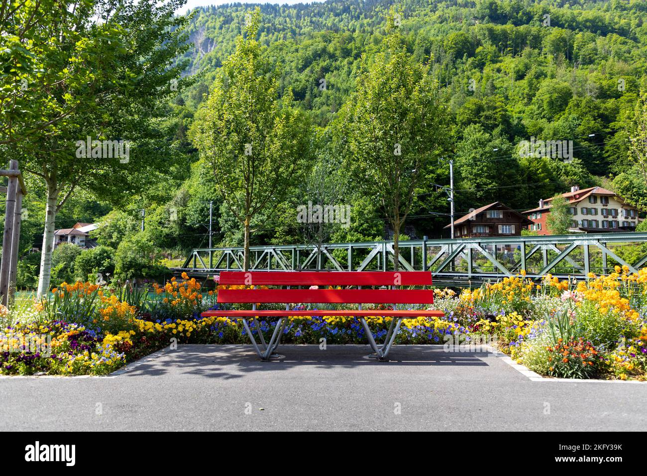 Banc de parc rouge entouré de fleurs printanières et de la forêt en arrière-plan dans la ville suisse d'Interlaken. Banque D'Images