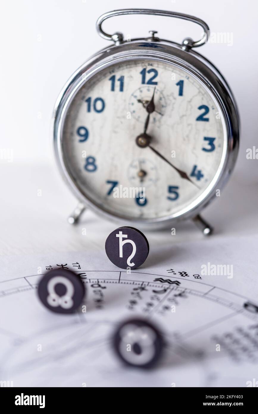 Un symbole zodiacal Saturne sur un dessin d'une carte natale et un arrière-plan défoqué d'une horloge Banque D'Images