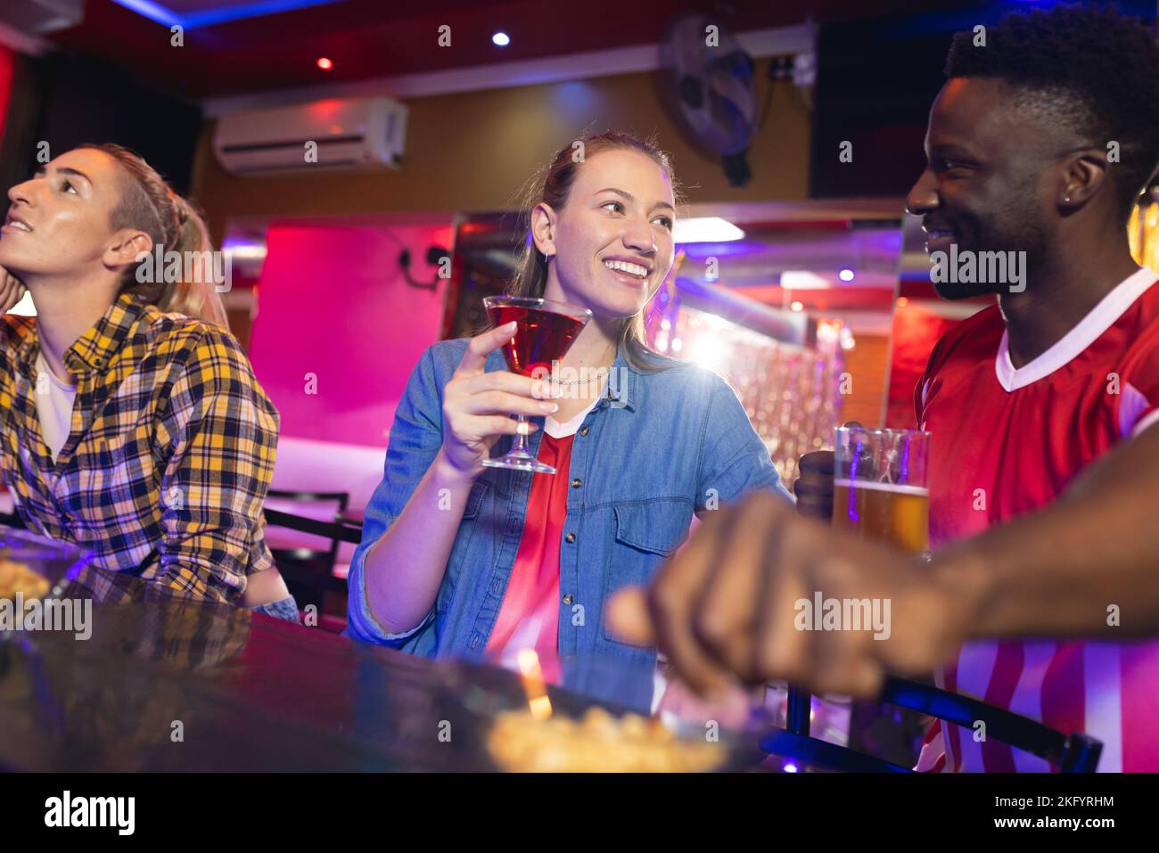 Groupe diversifié d'amis heureux de sexe féminin et masculin regardant un match sportif, parlant et buvant dans un bar Banque D'Images