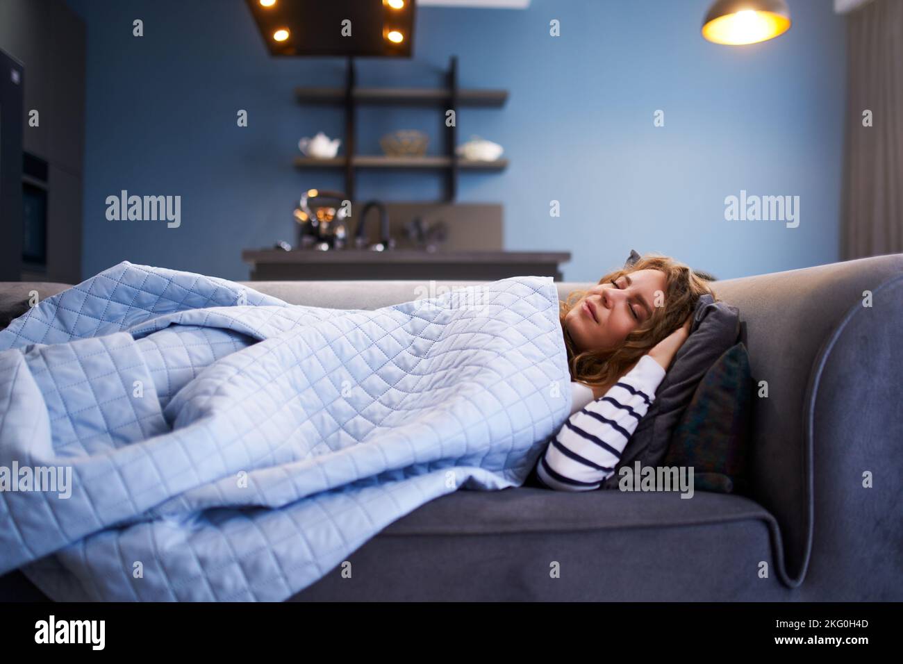 Une fille dort sur un canapé confortable dans la salle de séjour à l'heure de la sieste sous une couverture chaude. Femme dormant prenant la sieste sur le canapé pendant la journée. Banque D'Images