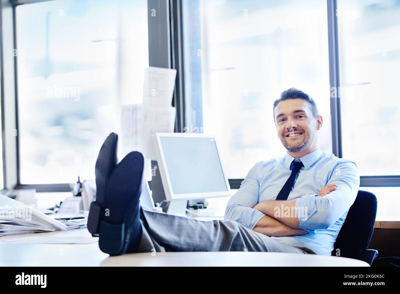 Le travail ne vaut pas mieux que cela. Portrait d'un homme d'affaires souriant assis avec ses pieds sur son bureau. Banque D'Images