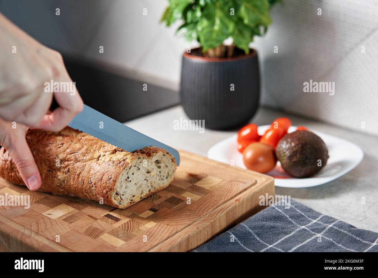 Femme coupant du pain de grain entier avec un grand couteau sur la planche à découper. Tranchez du pain frais et croustillant aux mains dans la cuisine Banque D'Images