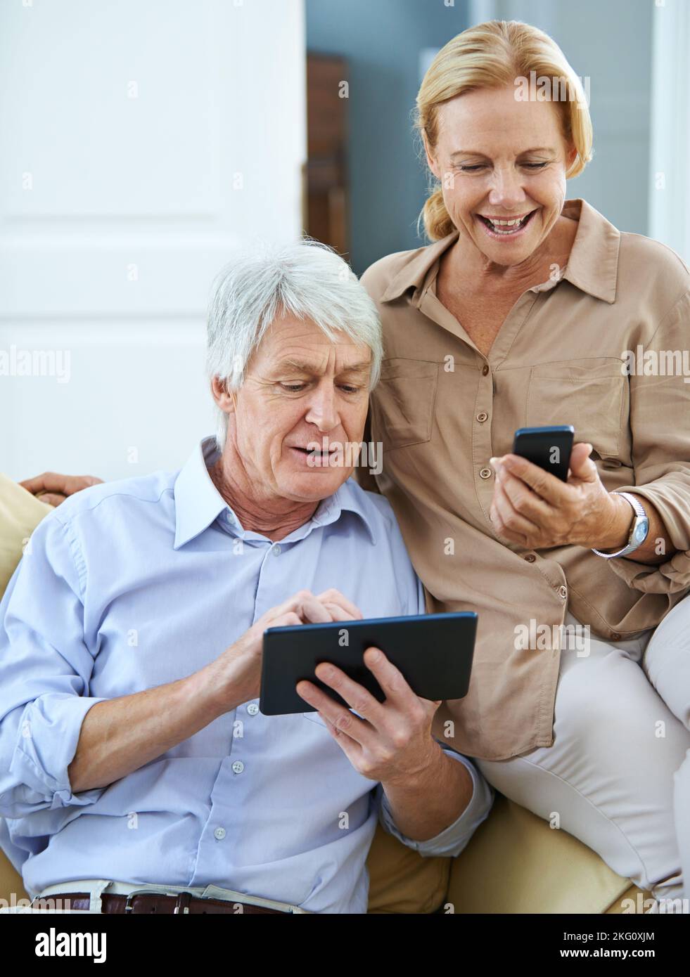 Mobilité moderne. Un homme âgé heureux utilisant une tablette numérique tandis que sa femme lit un message texte sur son téléphone portable. Banque D'Images