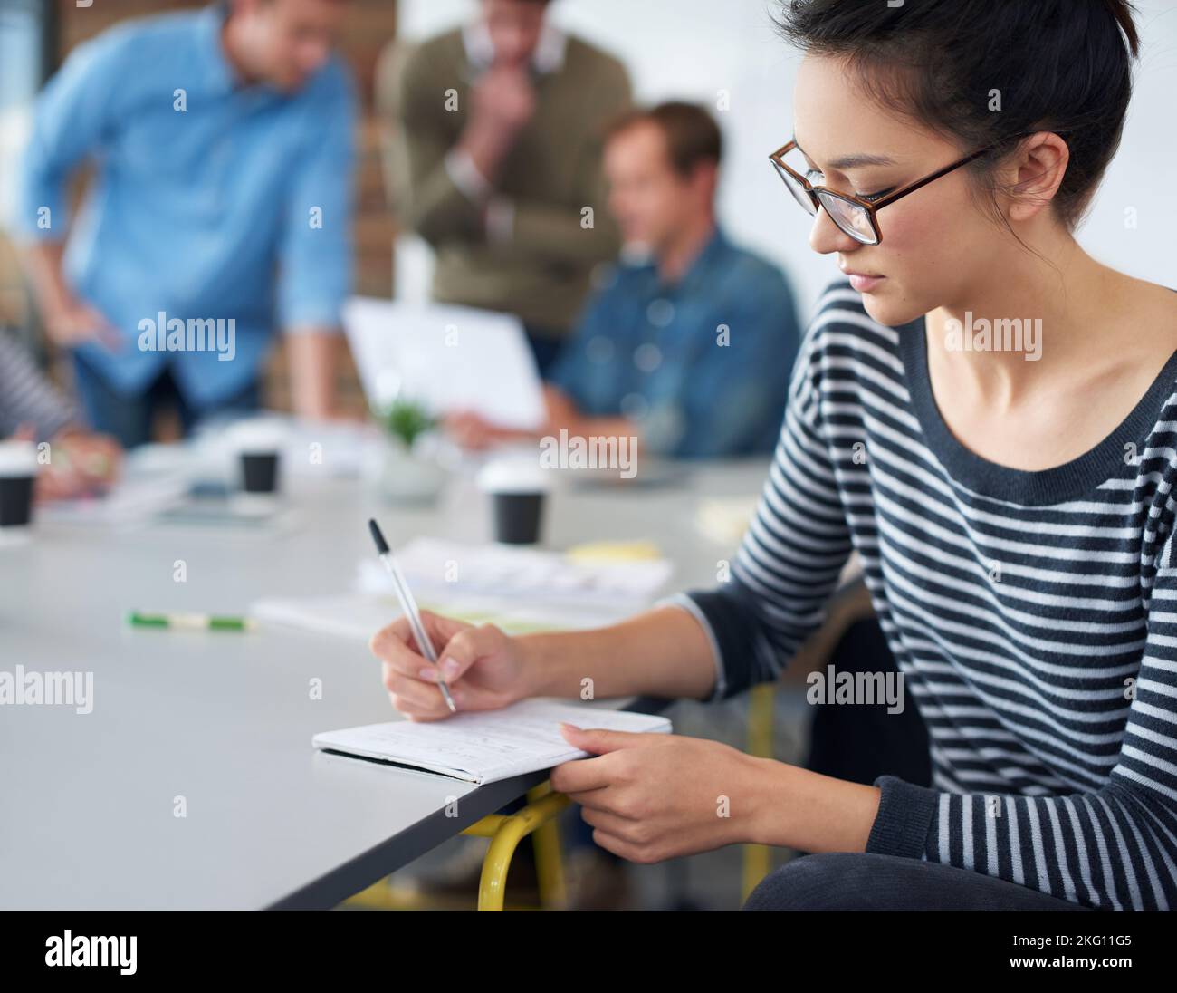 Stratégies de planification. Une jeune femme attrayante travaillant dans un bureau avec des collègues en arrière-plan. Banque D'Images