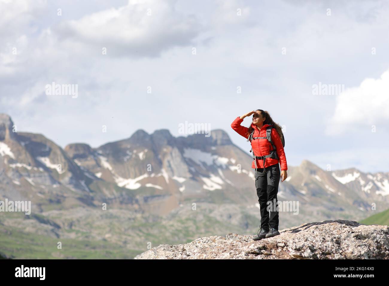 Portrait complet d'un randonneur en rouge cherchant à protéger du soleil avec sa main en haut de la montagne Banque D'Images