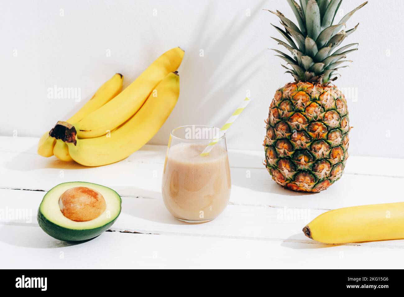 Encore la vie avec des fruits, des bananes, de l'ananas et des smoothie d'avocat sur une table en bois blanc avec de longues ombres. Concept de régime minimal de détox, vitamine dri d'été Banque D'Images