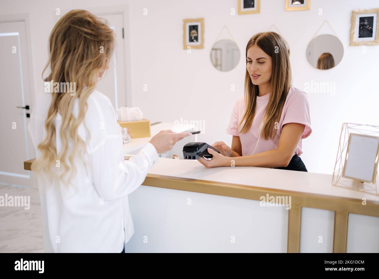 Les femmes paient pour les procédures dans le studio de beauté. Le caissier tient la main avec le lecteur de carte de crédit pendant que le client tient le téléphone pour le paiement NFC Banque D'Images
