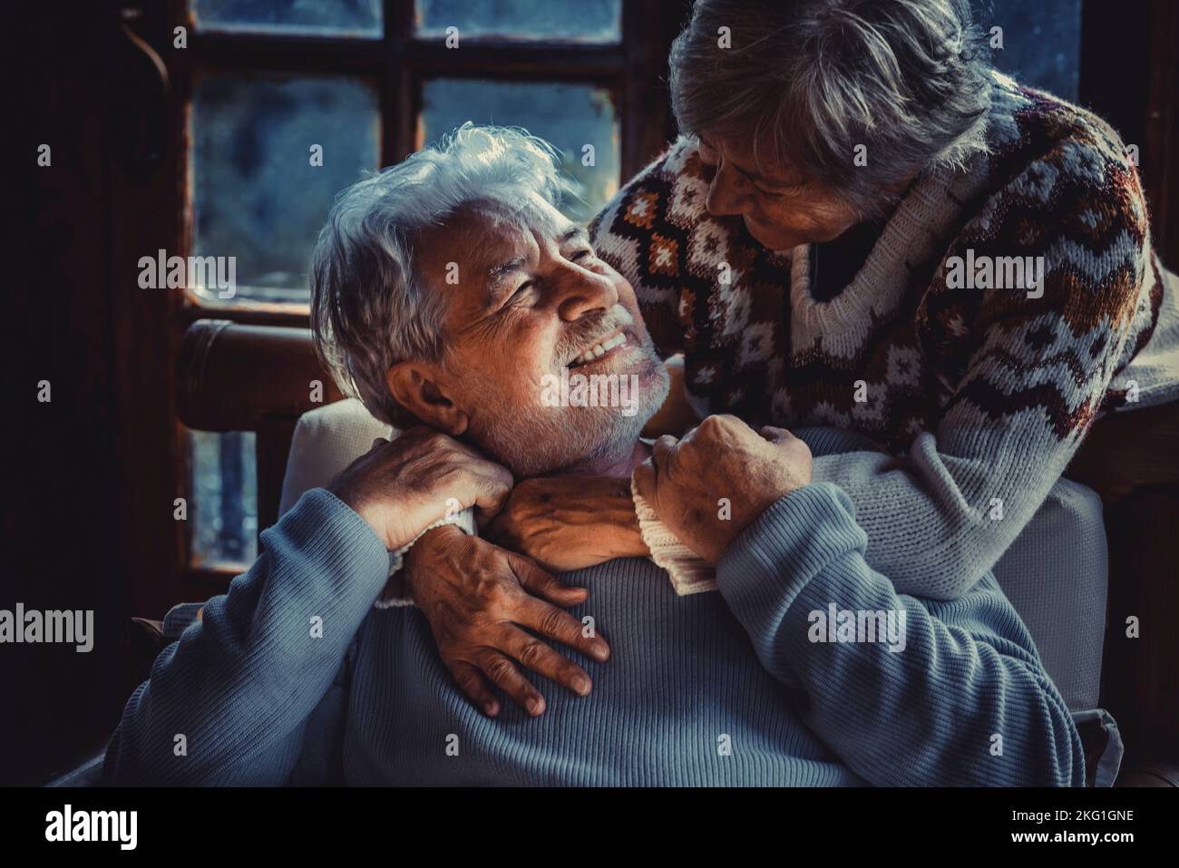 Portrait de deux personnes âgées amoureuses à la maison dans la lumière sombre du soir. L'homme âgé sourit à sa femme mûre embrassant et appréciant relationshi Banque D'Images