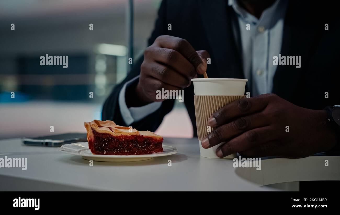 Homme d'affaires africain méconnu, homme d'affaires en costume formel, assis à table dans le café restaurant cafétéria, mélange le sucre dans une tasse de thé de café aromatique Banque D'Images