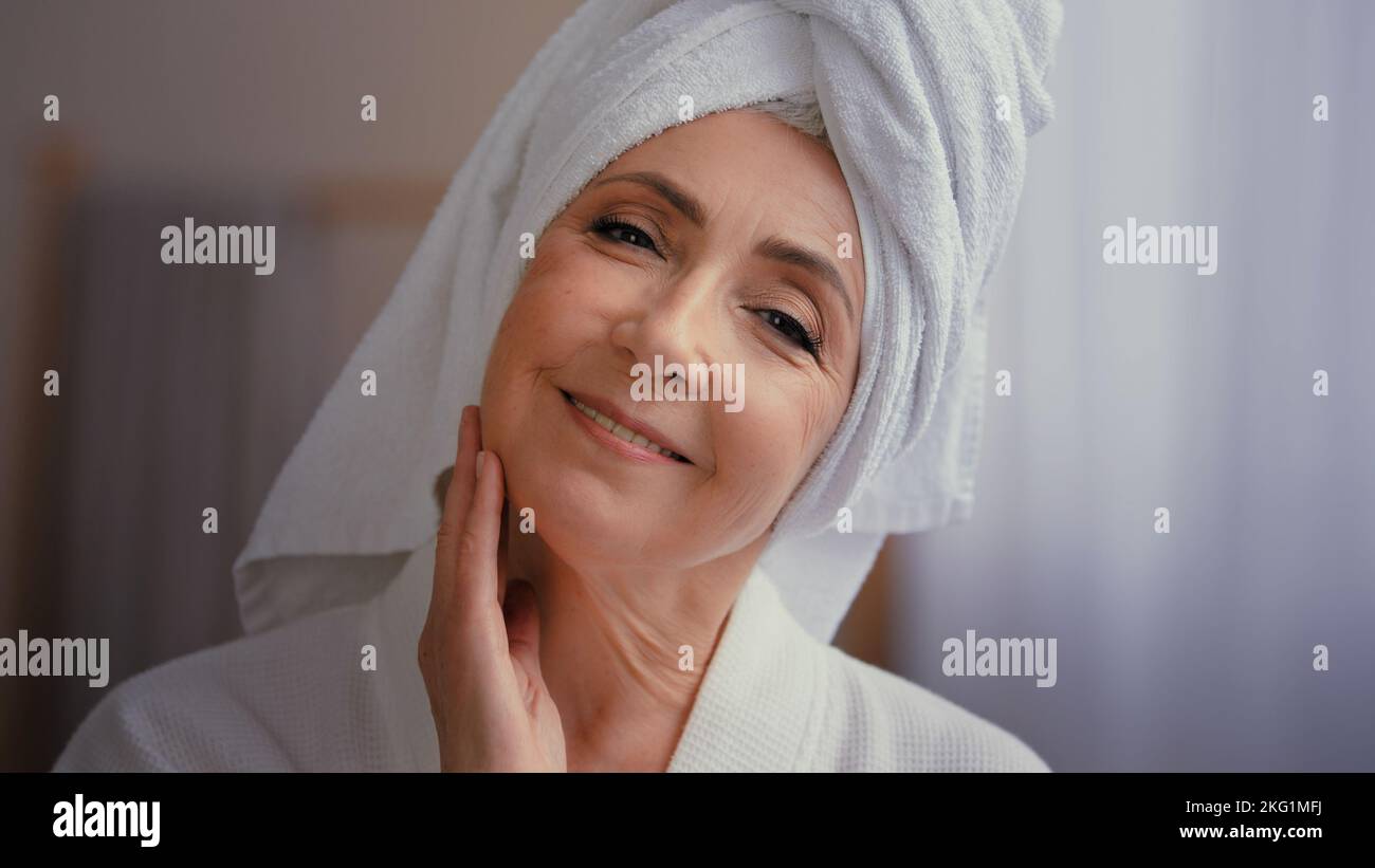 Gros plan portrait de femme heureuse 50s femme d'âge moyen 60s femme mûre touchant la peau du visage regardant l'appareil photo avec sourire toucher visage se faire dorloter s'use Banque D'Images