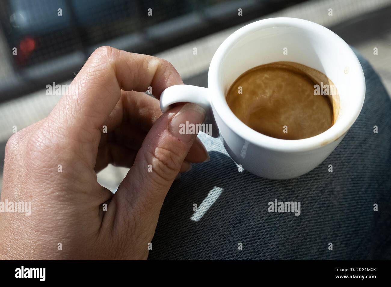 Main humaine avec une petite tasse de café espresso blanc et vide, au soleil éclatant. Moment de méditation. Frein à café. Banque D'Images