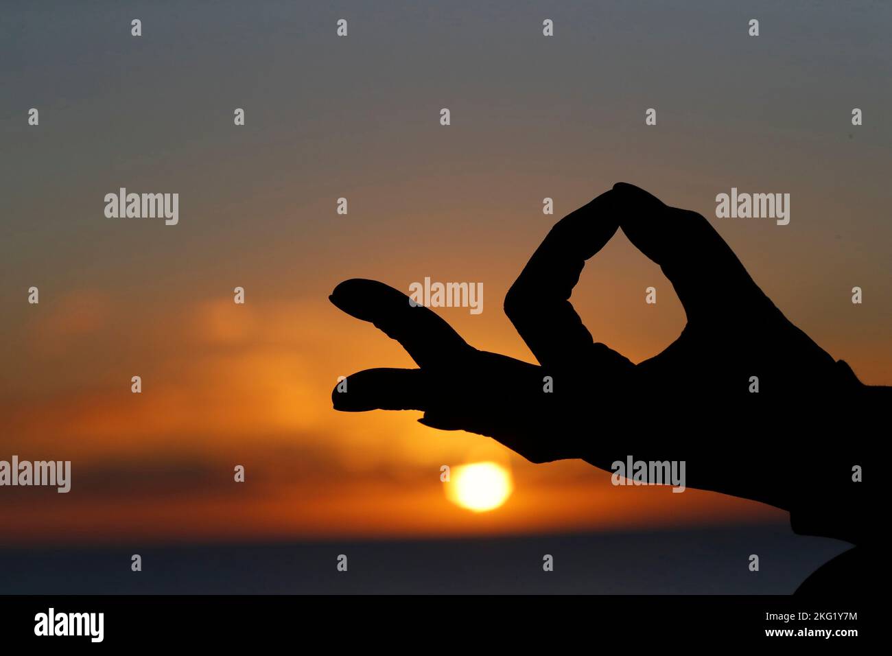 Femme pratiquant la méditation de yoga par la mer au coucher du soleil comme concept de silence et de détente. Gros plan sur la main, gyan mudra. Banque D'Images