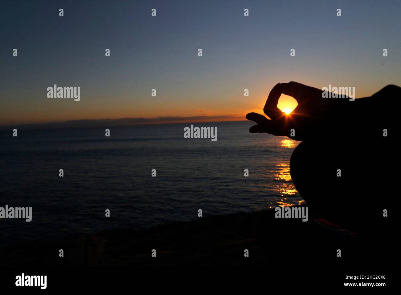 Femme pratiquant la méditation de yoga par la mer au coucher du soleil comme concept de silence et de détente. Gros plan sur la main, gyan mudra. Banque D'Images