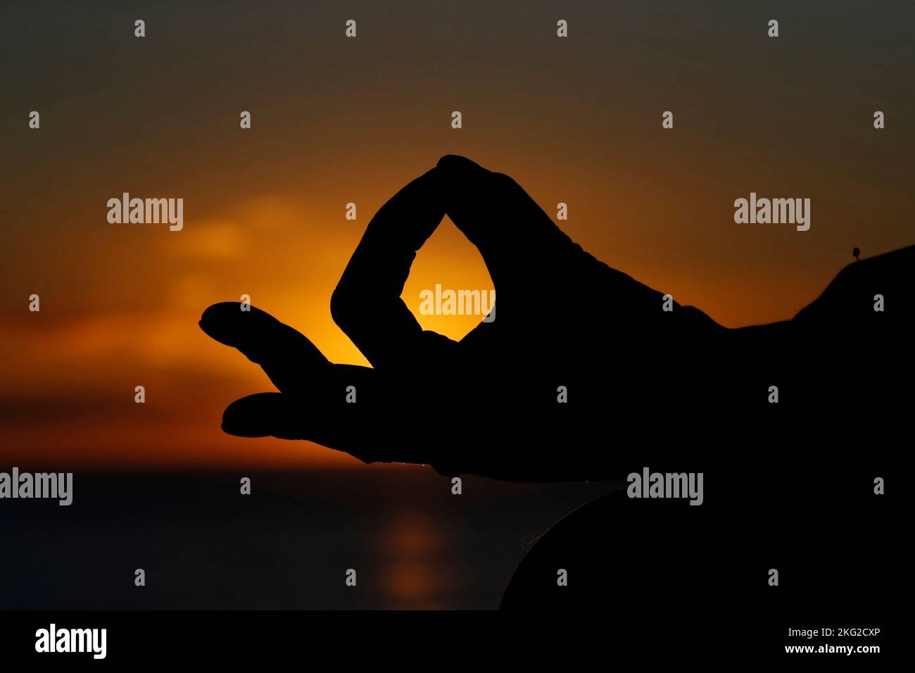 Femme pratiquant la méditation de yoga par la mer au coucher du soleil comme concept de silence et de détente. Gros plan sur la main, gyan mudra. Banque D'Images