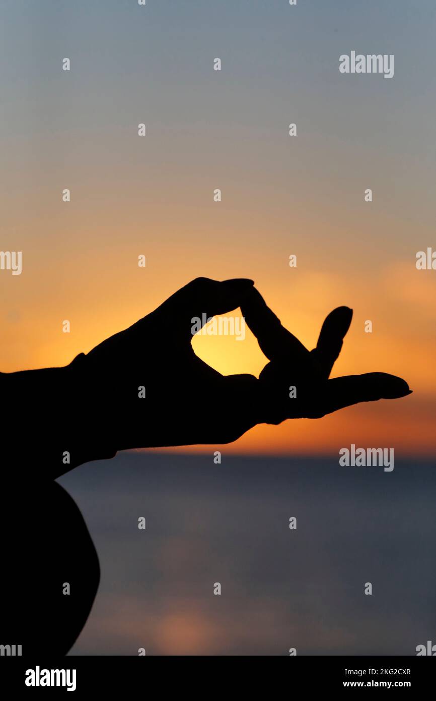 Femme pratiquant la méditation de yoga par la mer au coucher du soleil comme concept de silence et de détente. Gros plan sur la main, gyan mudra. Banque D'Images