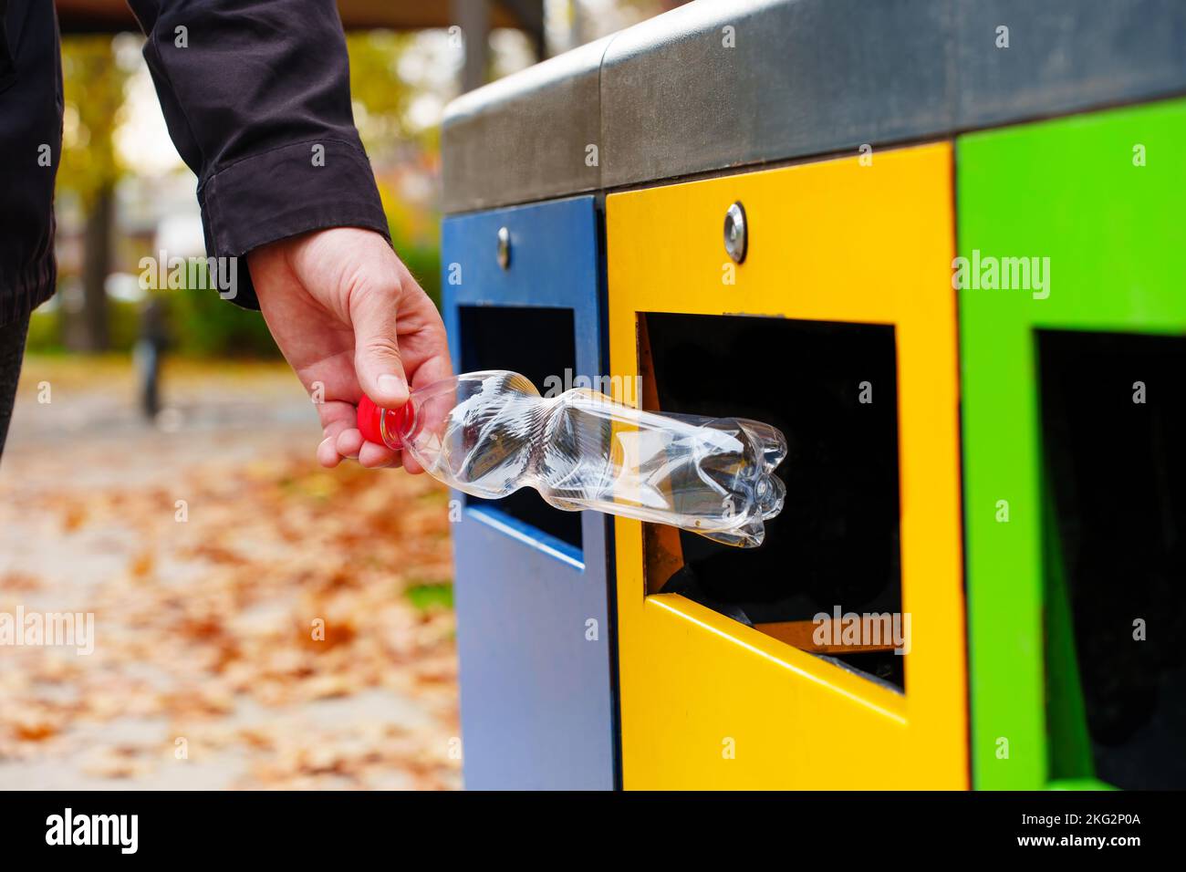 Un homme lance une bouteille en plastique dans une poubelle jaune dans le parc local. Concept responsable du tri, de la collecte et du recyclage des déchets. Banque D'Images