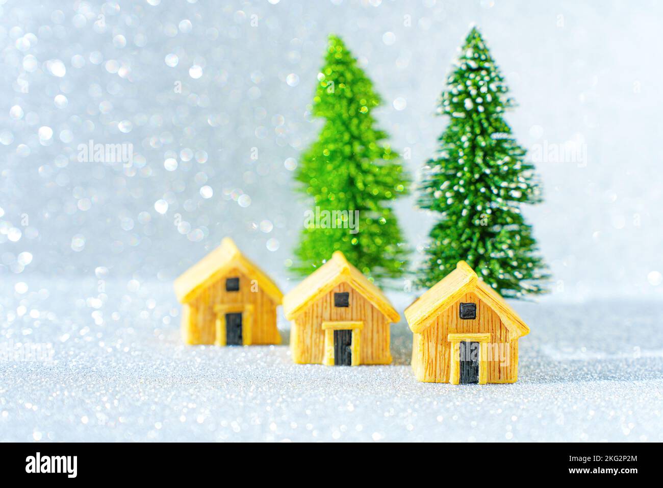 Trois cottages miniatures et deux arbres de Noël sur fond étincelant. Banque D'Images