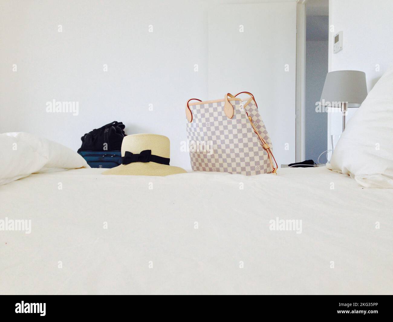 Un chapeau de paille de plage et un sac Louis Vuitton sur le linge blanc du  lit Photo Stock - Alamy
