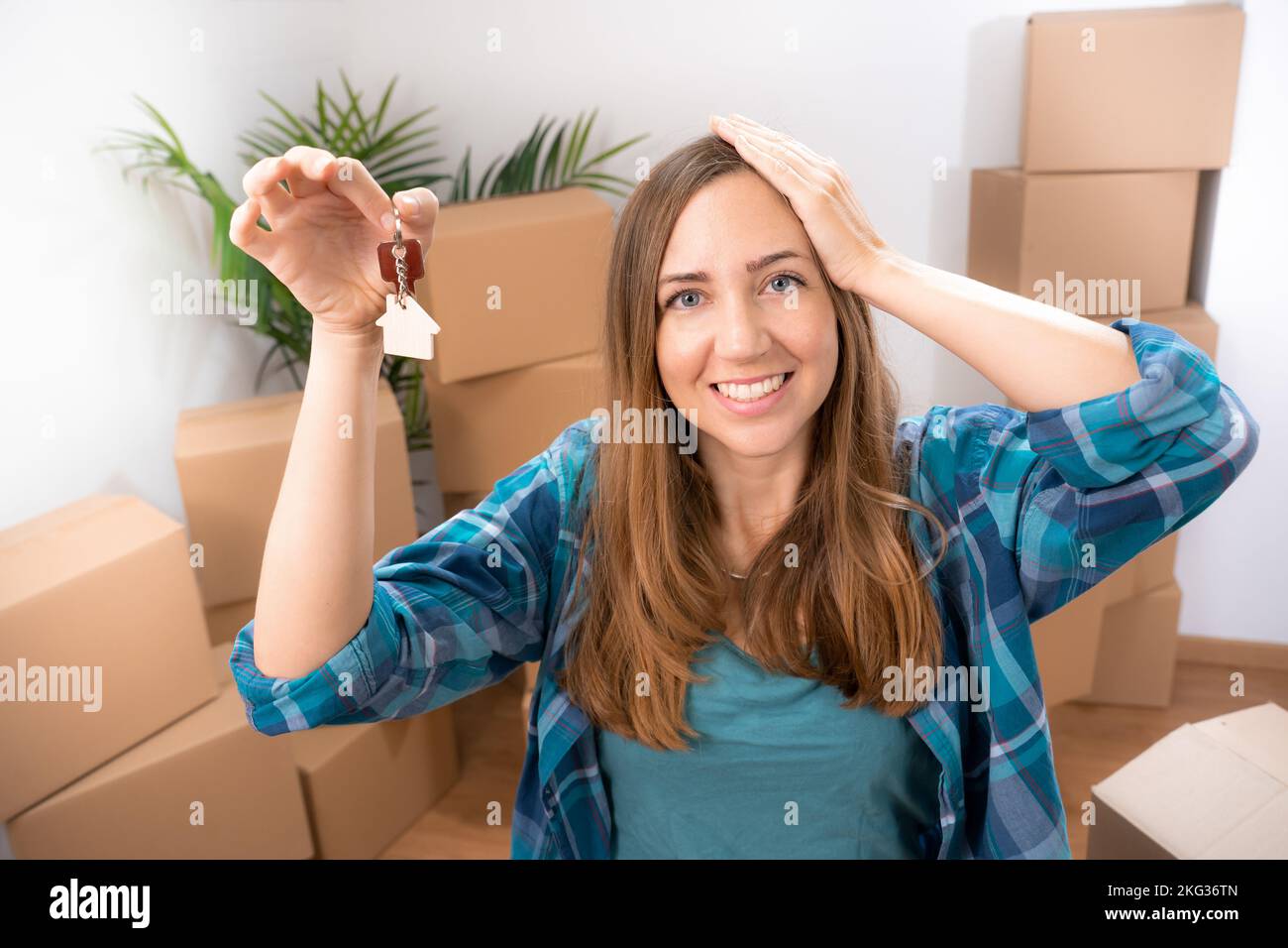Une femme excitée souriant avec les nouvelles clés de la maison sa main sur la tête dans sa nouvelle maison vide avec des boîtes Banque D'Images