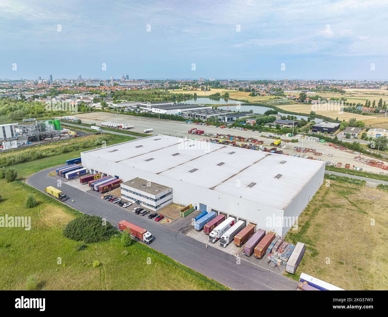 Vue aérienne de dessus de l'usine industrielle entourée d'une végétation luxuriante et de camions garés dans la baie de chargement Banque D'Images
