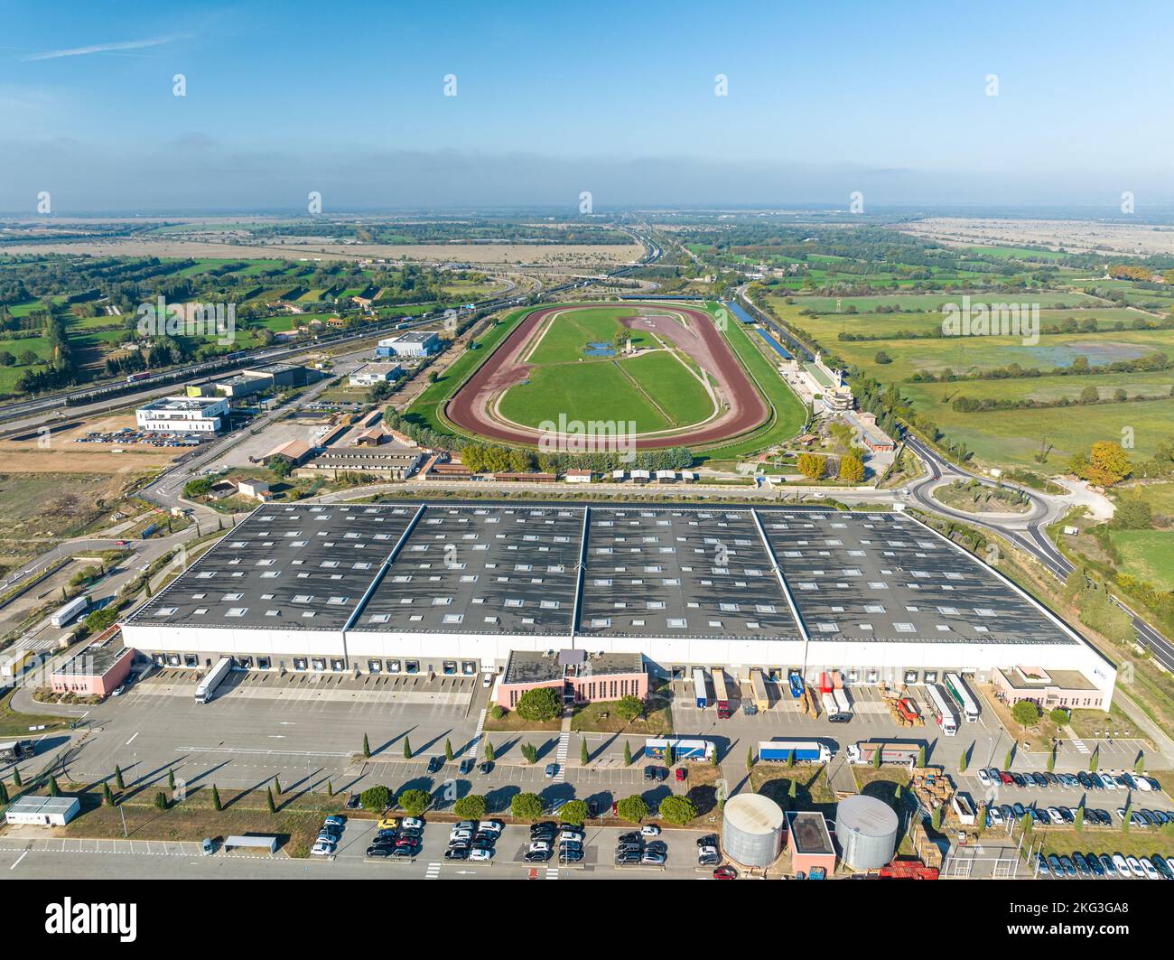 Plan aérien de l'entrepôt avec des camions garés dans la baie de chargement avec parking personnel, un terrain de sport ovale avec verdure Banque D'Images