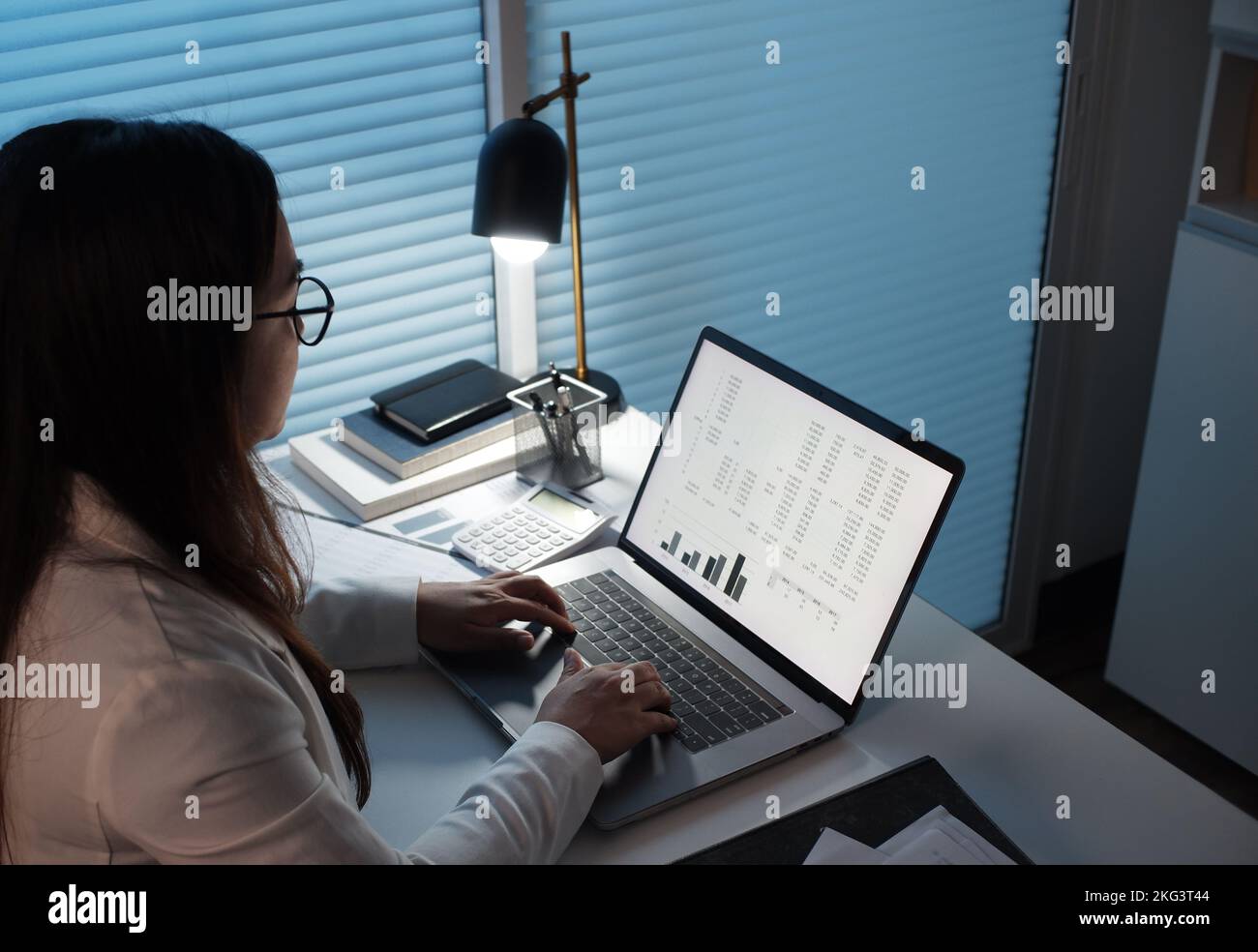 Jeunes femmes asiatiques travaillant tard dans la nuit dans une pièce sombre, utilisant un ordinateur portable. Banque D'Images