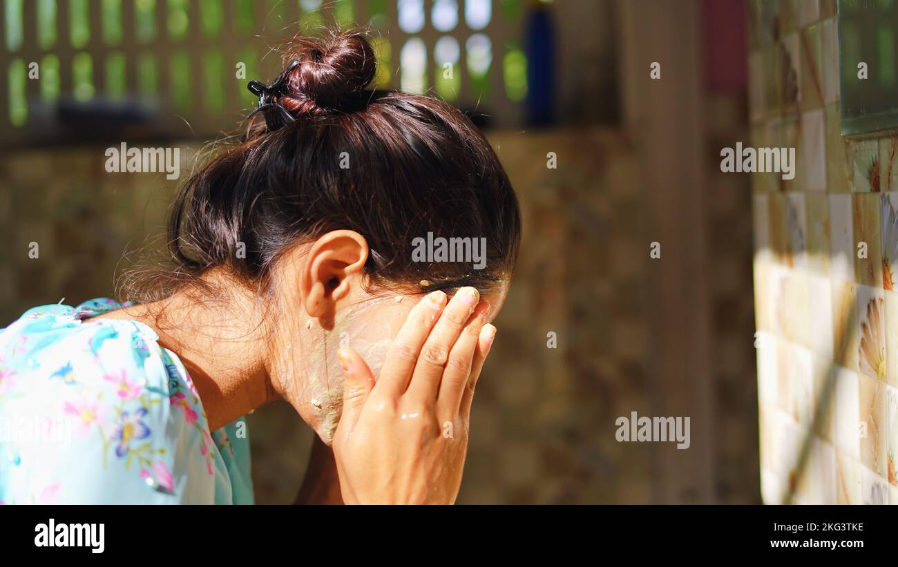 Une belle femme est de laver le masque facial dans la salle de bains après avoir appliqué le masque facial. Fille pulvérisant de l'eau sur son visage debout devant le miroir à la maison. um Banque D'Images