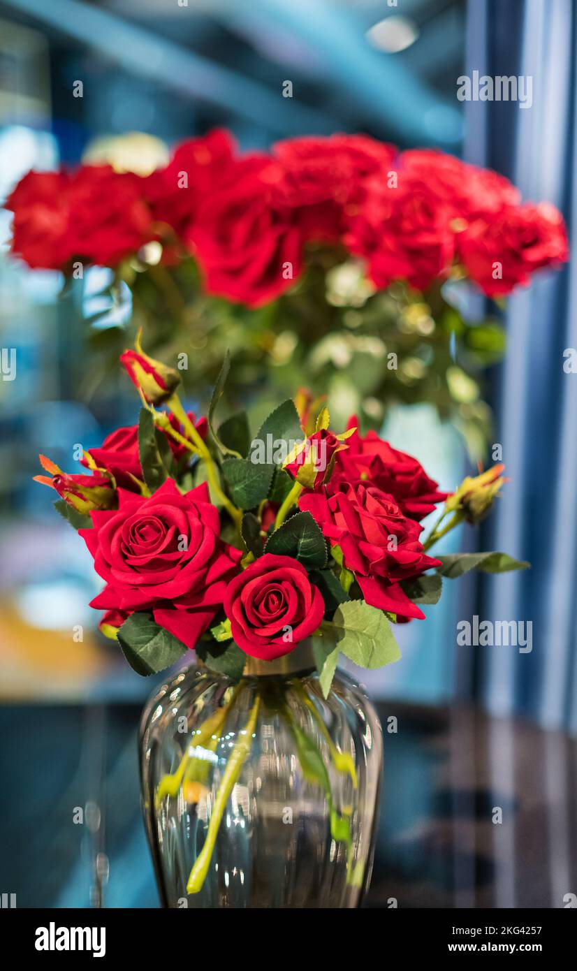 Bouquet de roses fraîches avec des pétales rouges placés dans un vase en verre sur fond flou Banque D'Images