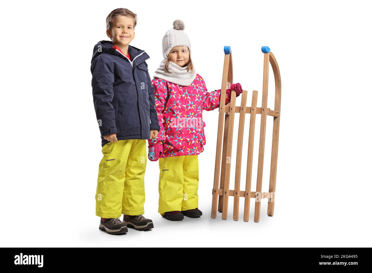 Enfants en vêtements d'hiver debout avec un traîneau en bois isolé sur fond blanc Banque D'Images