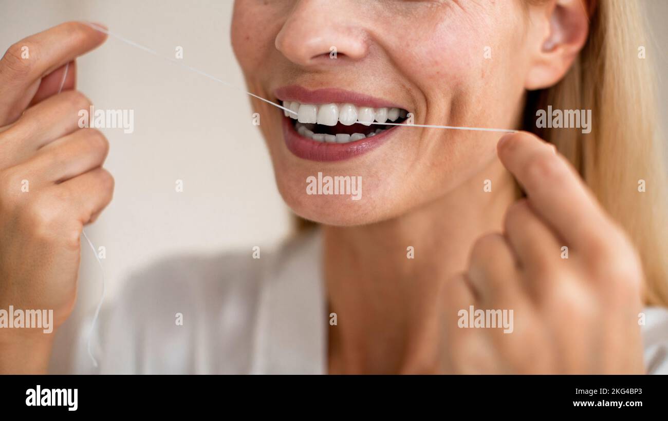 Concept de soins de la bouche et de soins de la bouche. Gros plan coupe courte d'une femme d'âge moyen non reconnaissable utilisant une soie dentaire Banque D'Images
