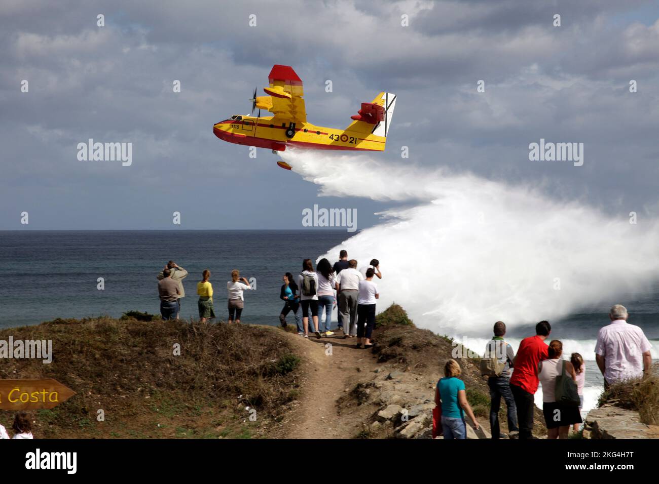 Petit avion pompier jetant de l'eau devant la côte avec des gens qui l'observent. Playa de las Catedrales, Galice, Ribadeo, Lugo, Espagne. Banque D'Images