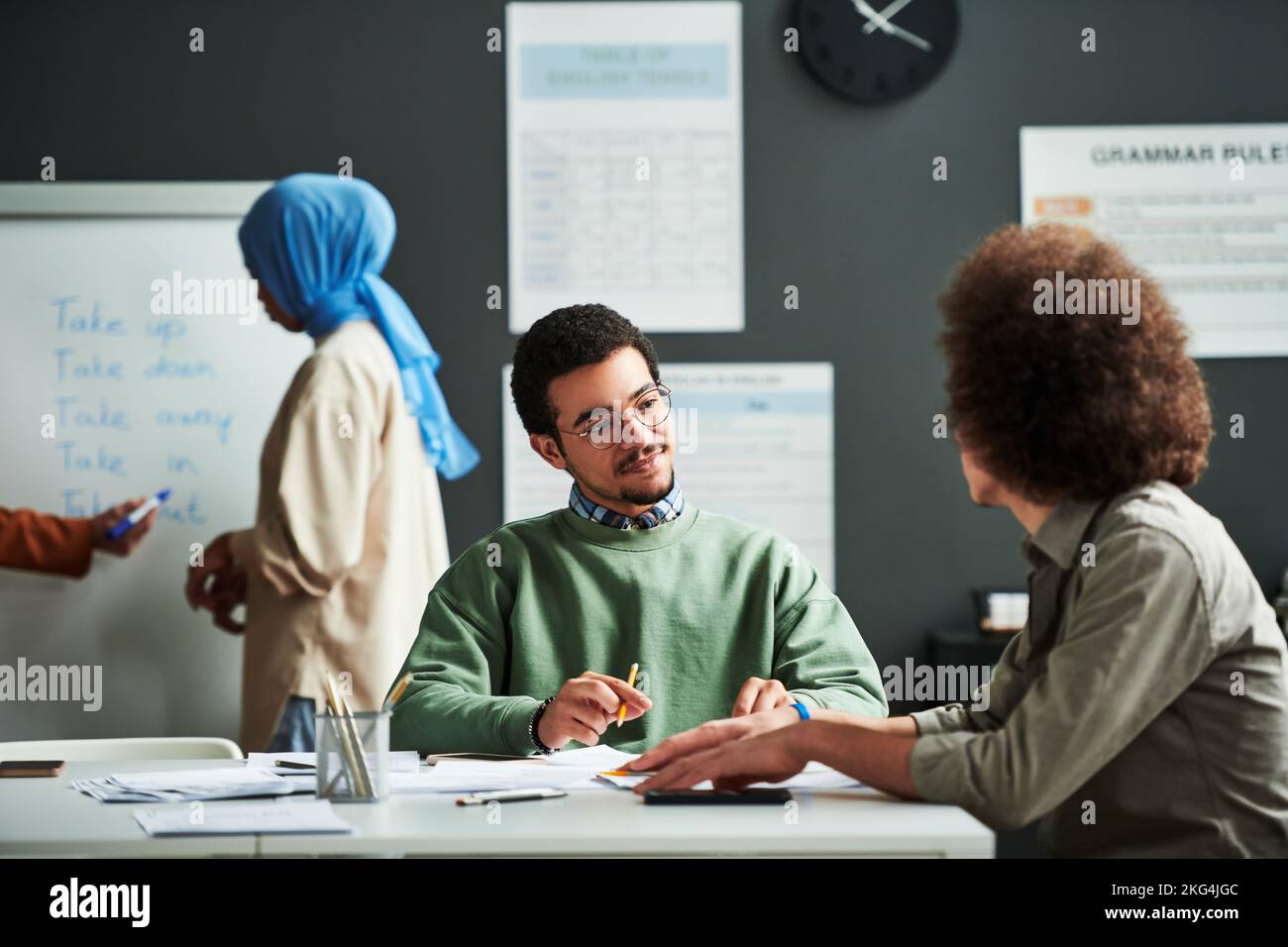 Homme du Moyen-Orient confiant regardant le camarade de classe et l'écoutant en leçon contre une jeune étudiante musulmane en hijab bleu Banque D'Images