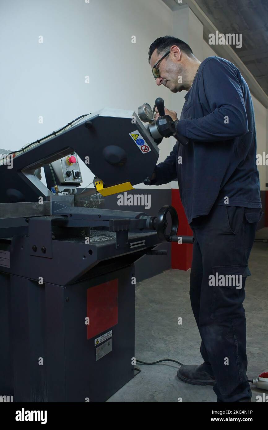 homme mature travaillant et coupant du métal avec une scie industrielle en atelier Banque D'Images