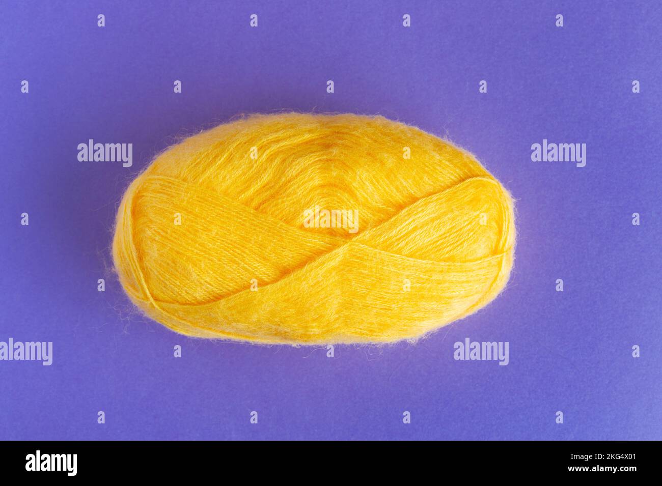 Rouleau de fils de laine jaune pour tricoter sur fond violet et lilas. Banque D'Images