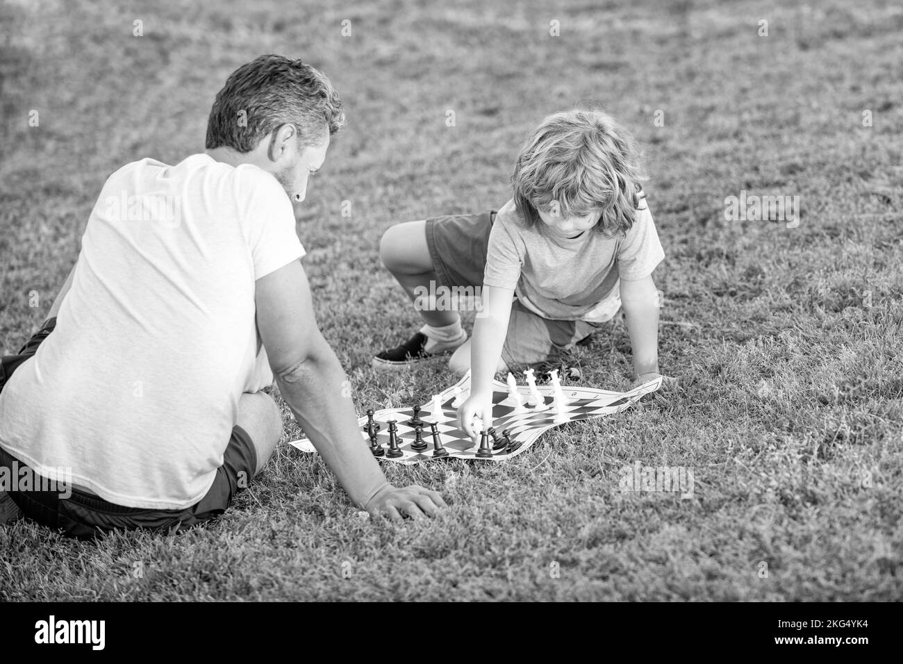père et fils jouant aux échecs sur l'herbe dans le parc. fête des pères. bonne famille. la parentalité et l'enfance. checkmate. passer du temps ensemble. stratégique et t Banque D'Images