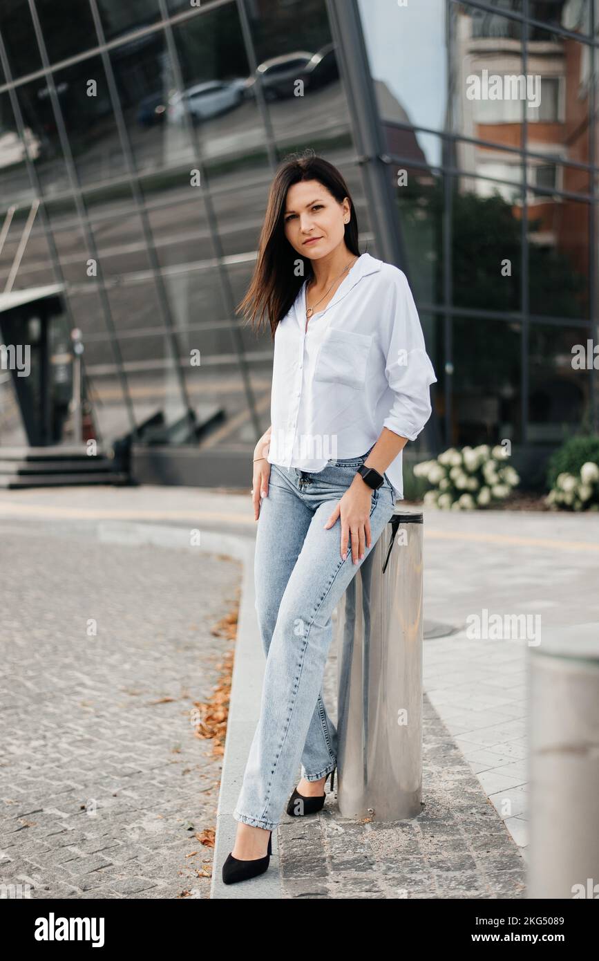 Une jeune femme pose près d'un bâtiment en jeans et d'un chemisier blanc. Banque D'Images