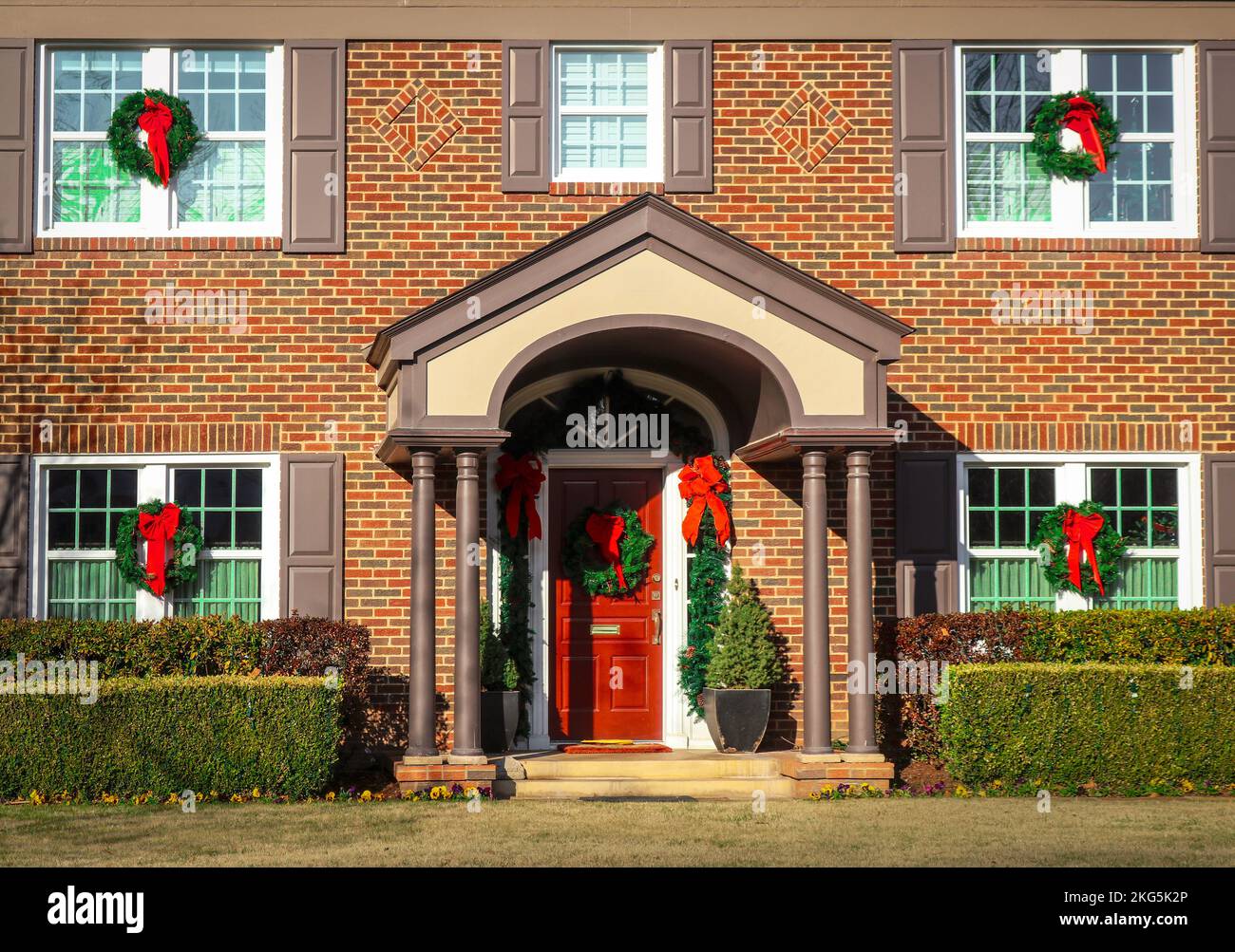 Entrée d'une maison en brique de deux étages avec porche voûté décoré pour Noël avec des couronnes sur les fenêtres et guirlande avec des rubans rouges Banque D'Images