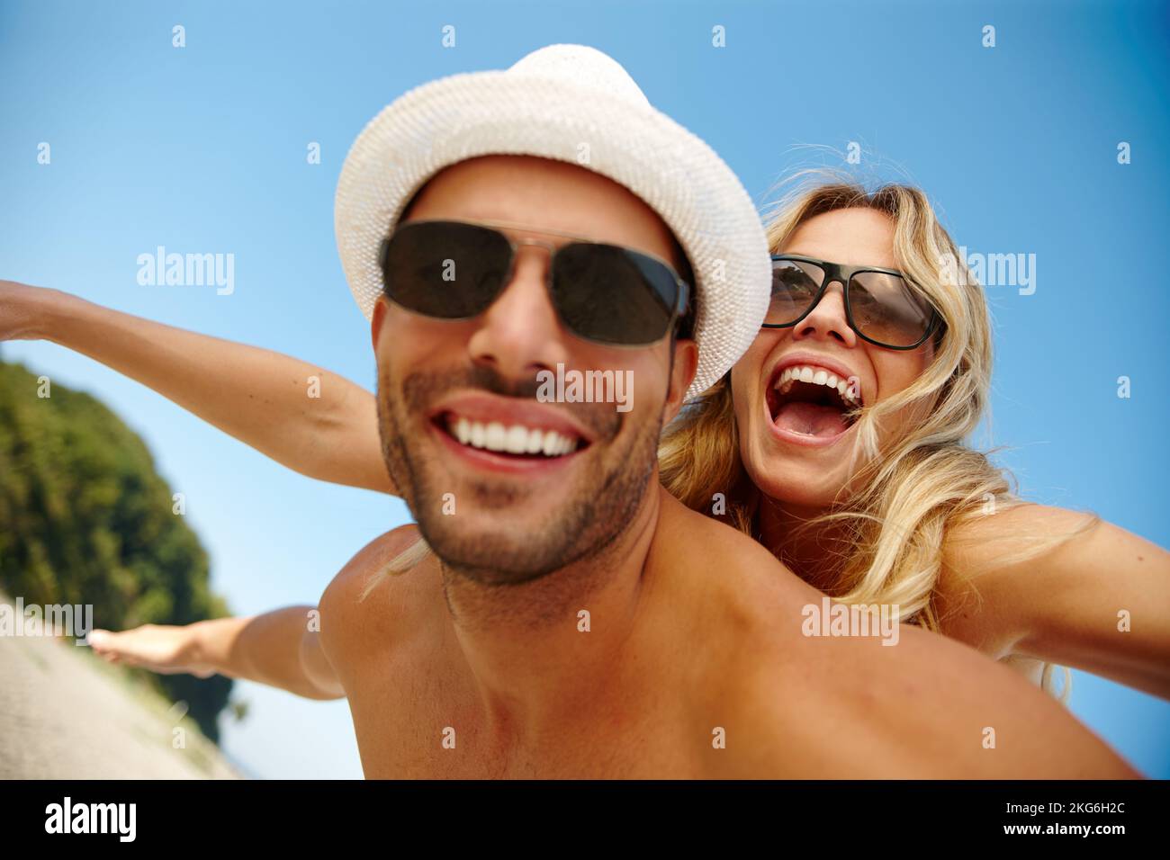 S'échapper de tout n'a jamais été aussi amusant. un jeune homme souriant donnant à sa petite amie en riant un porcyback sur une plage ensoleillée. Banque D'Images