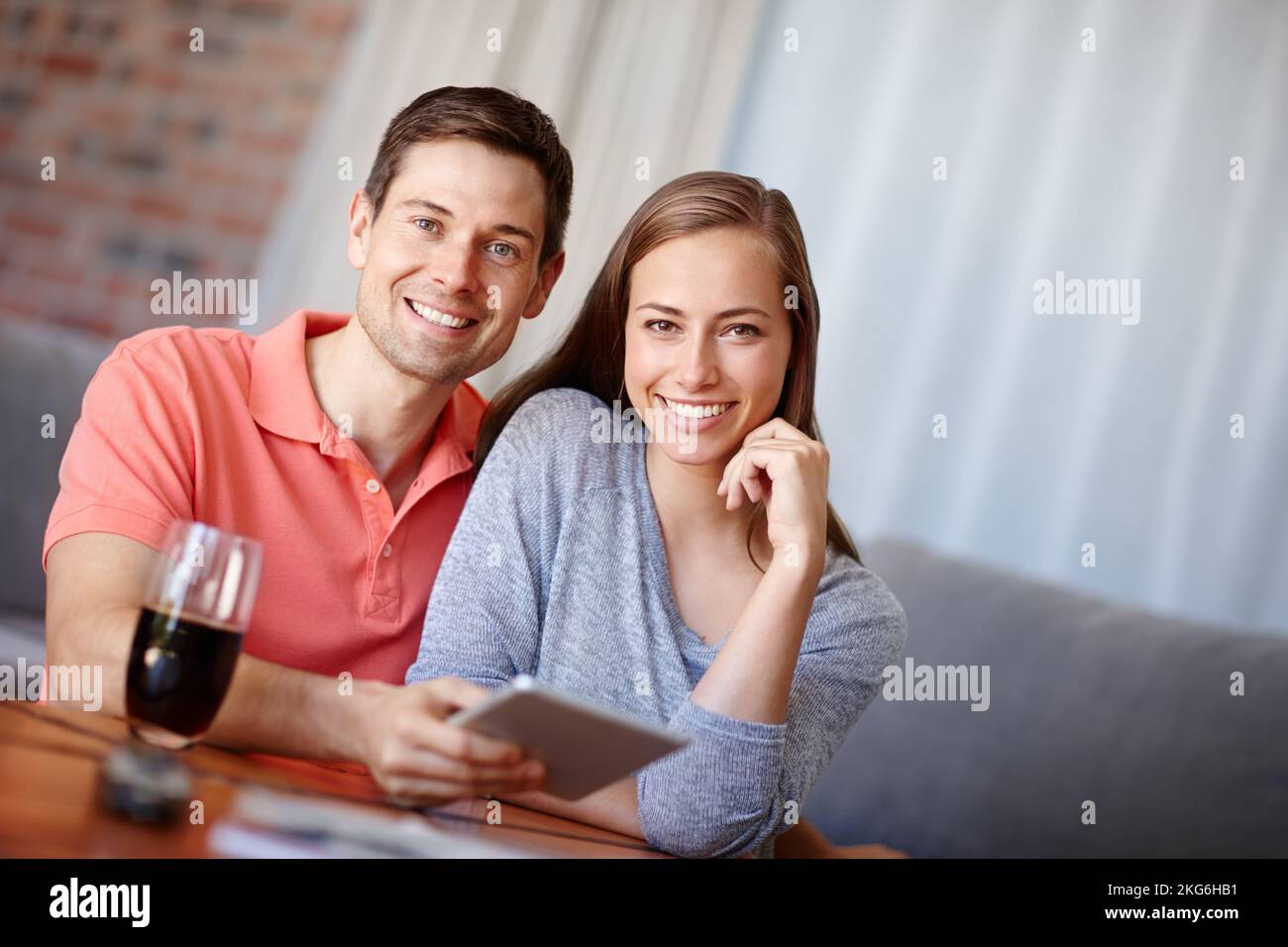 Album photo numérique à bord. Portrait d'un jeune couple souriant lorsqu'il utilise une tablette numérique à la maison. Banque D'Images