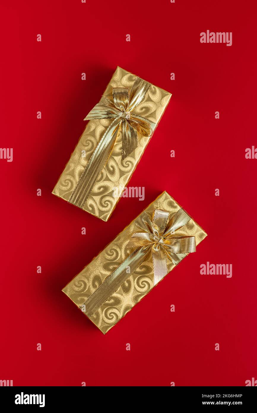 Cadeau emballé dans du papier d'aluminium doré. Cadeau de Noël avec ruban doré sur fond rouge. Vue de dessus. Banque D'Images