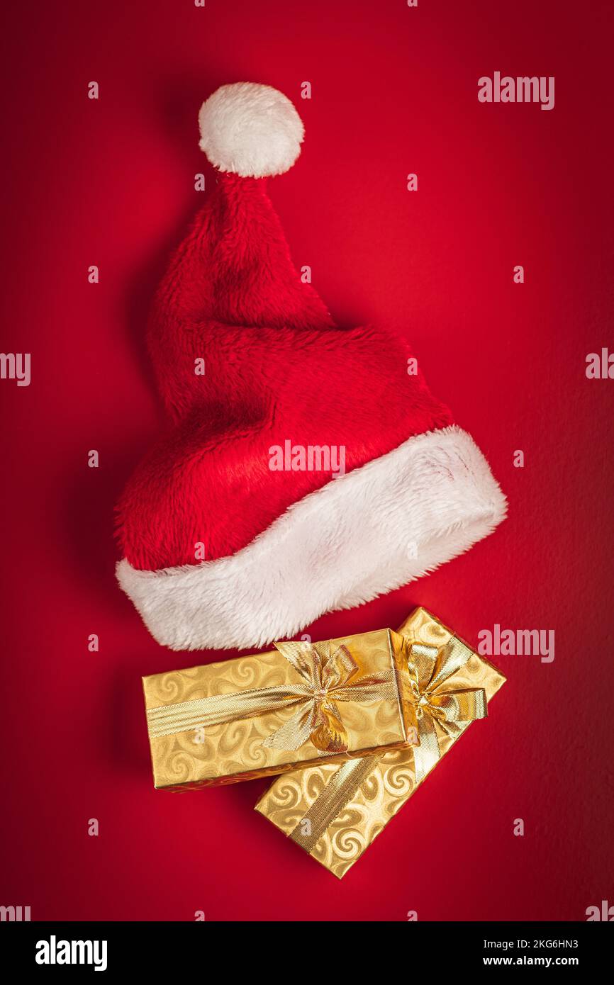 Cadeau de noël doré et chapeau de père Noël rouge sur fond rouge. Vue de dessus. Banque D'Images