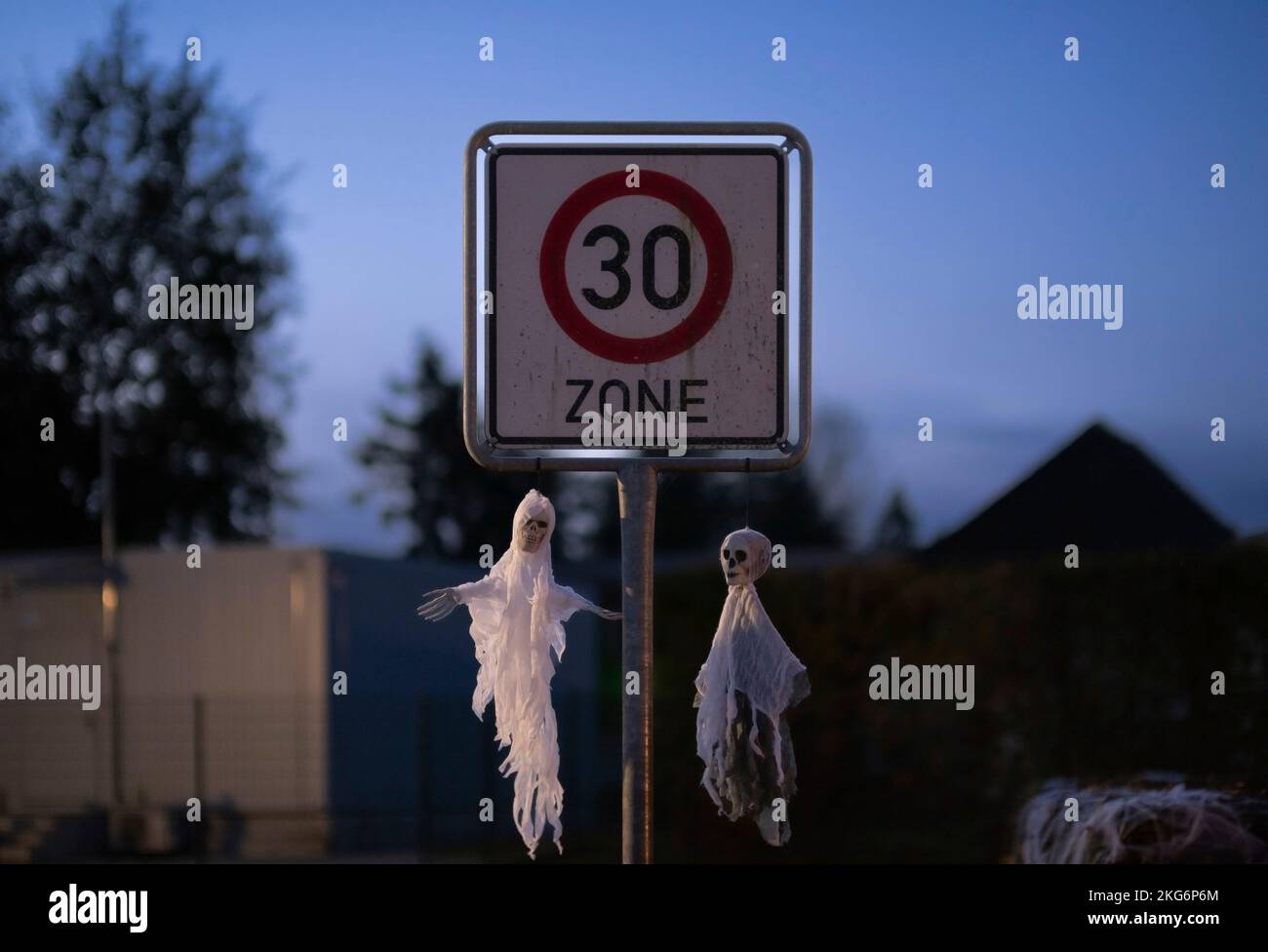 Décorations d'Halloween mettant en vedette deux mannequins fantômes accrochés à un panneau de limitation de vitesse dans une zone 30, créant une atmosphère effrayante et festive. Banque D'Images