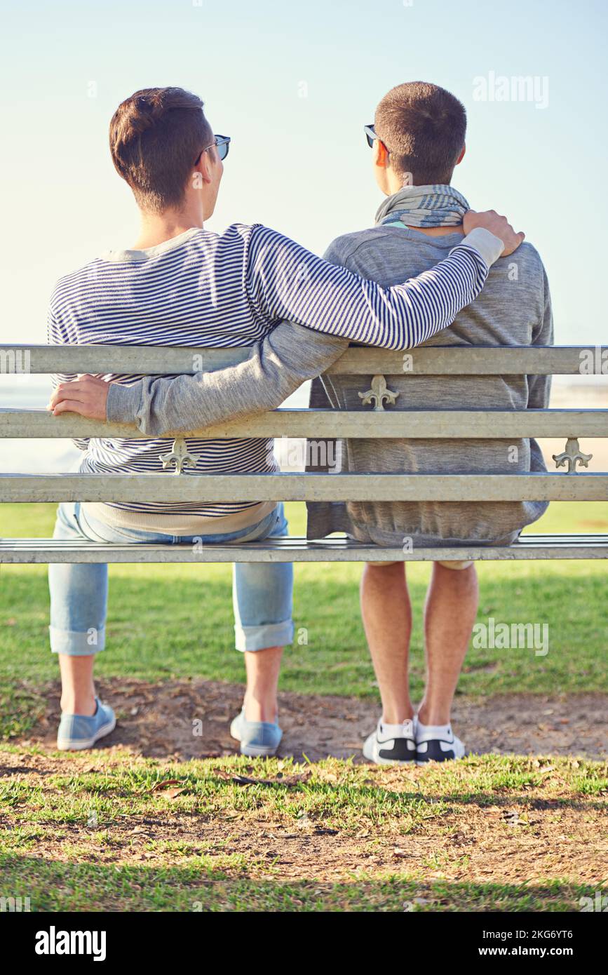 Prendre un après-midi romantique ensemble. Vue arrière d'un jeune couple gay assis ensemble sur un banc de parc. Banque D'Images