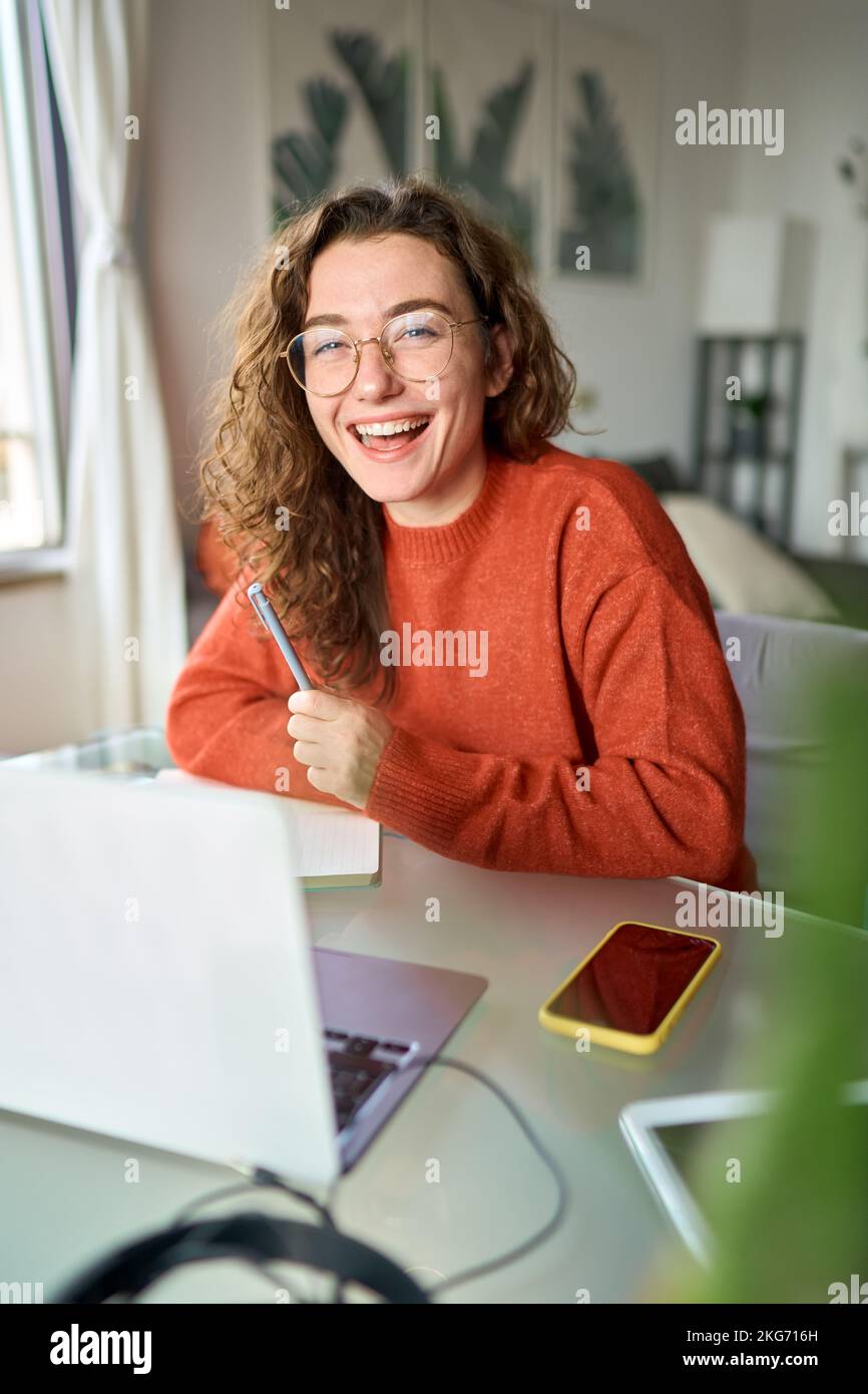 Une jeune étudiante heureuse riant en utilisant un ordinateur portable assis à son bureau étudiant en ligne. Banque D'Images