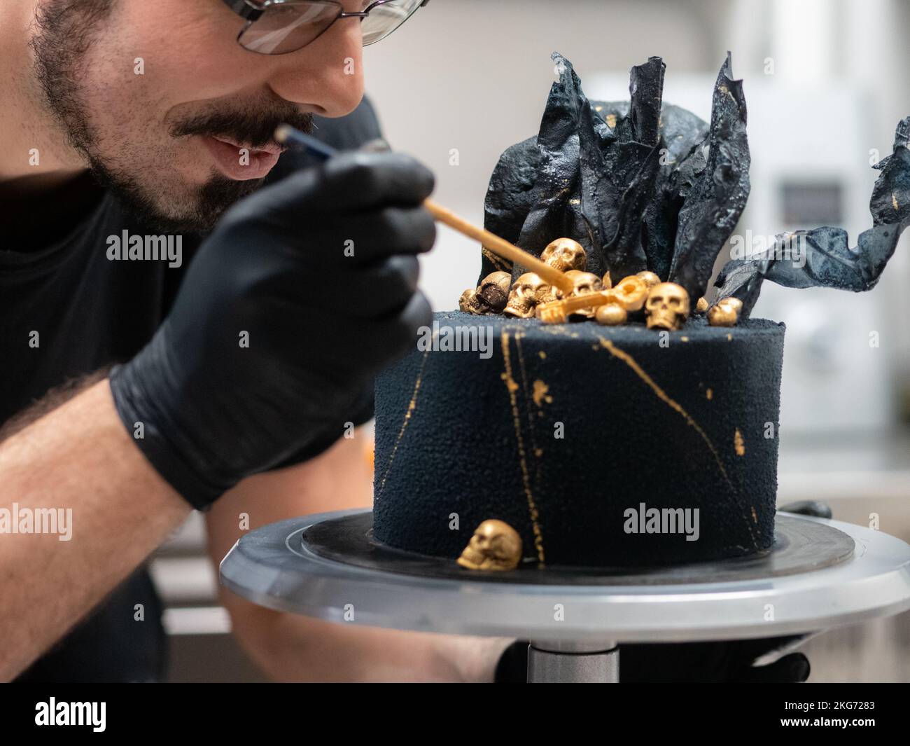 pâtissier finissant horreur gâteau d'anniversaire muertos noir décorant avec des crânes comestibles dorés et des voiles en papier de riz noir Banque D'Images