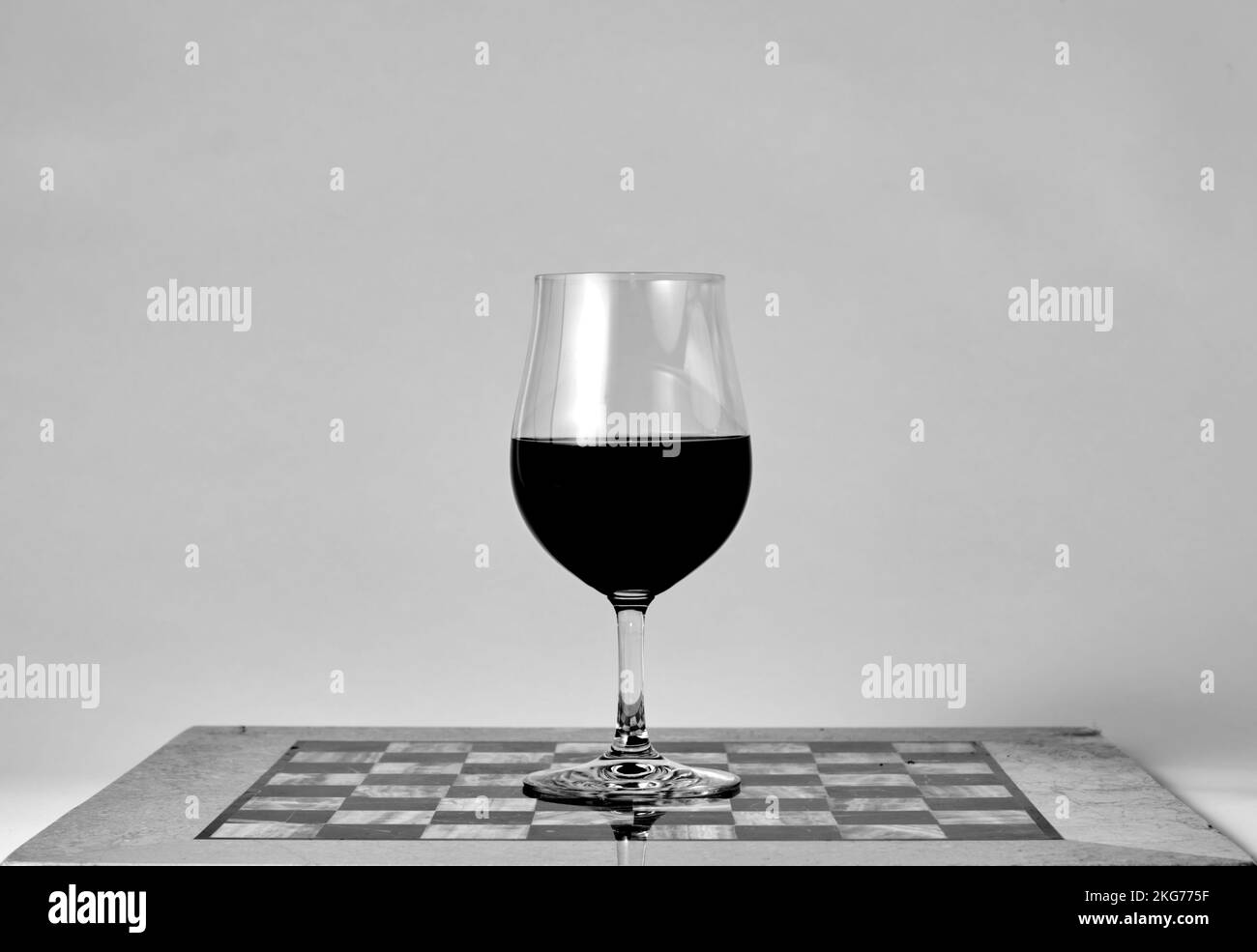 Verre à vin rouge debout sur l'échiquier. Macro gros plan sur fond blanc. Photo noir et blanc. Verres à vin. Jeu d'échecs. Banque D'Images