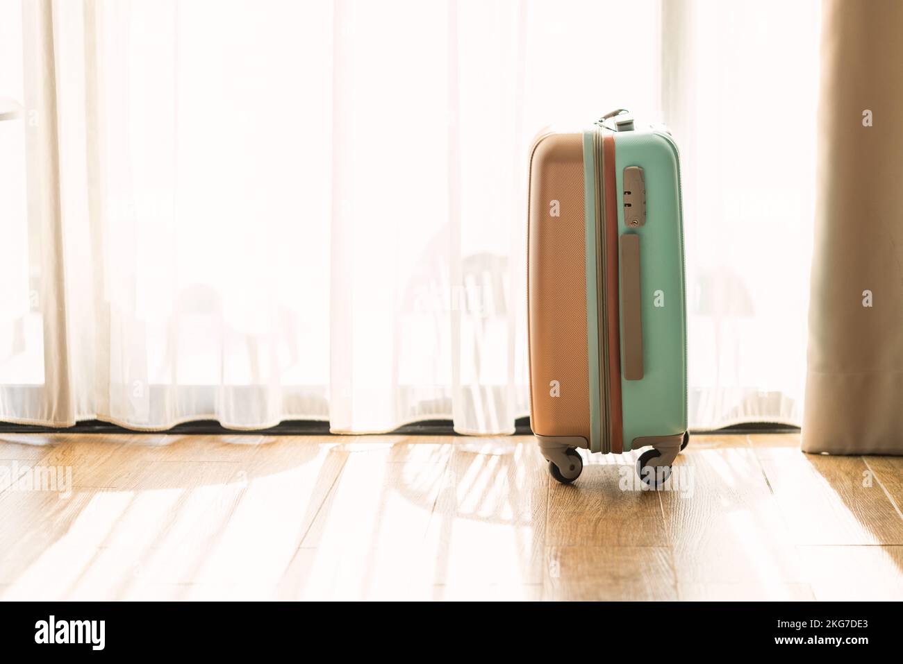 Vue latérale petit bagage moderne avec deux tons, se tenir sur le plancher en bois dans une chambre d'hôtel, arrière-plan de rideau blanc, espace pour le texte et le design. Banque D'Images